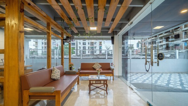 A modern interior with wooden beams, a glass wall, and a view of buildings outside. - Treebo Kashvijoy (Guwahati)