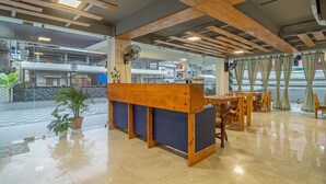 A reception area with a wooden counter, a fan, and a view of the street outside. - Treebo Kashvijoy (Guwahati)