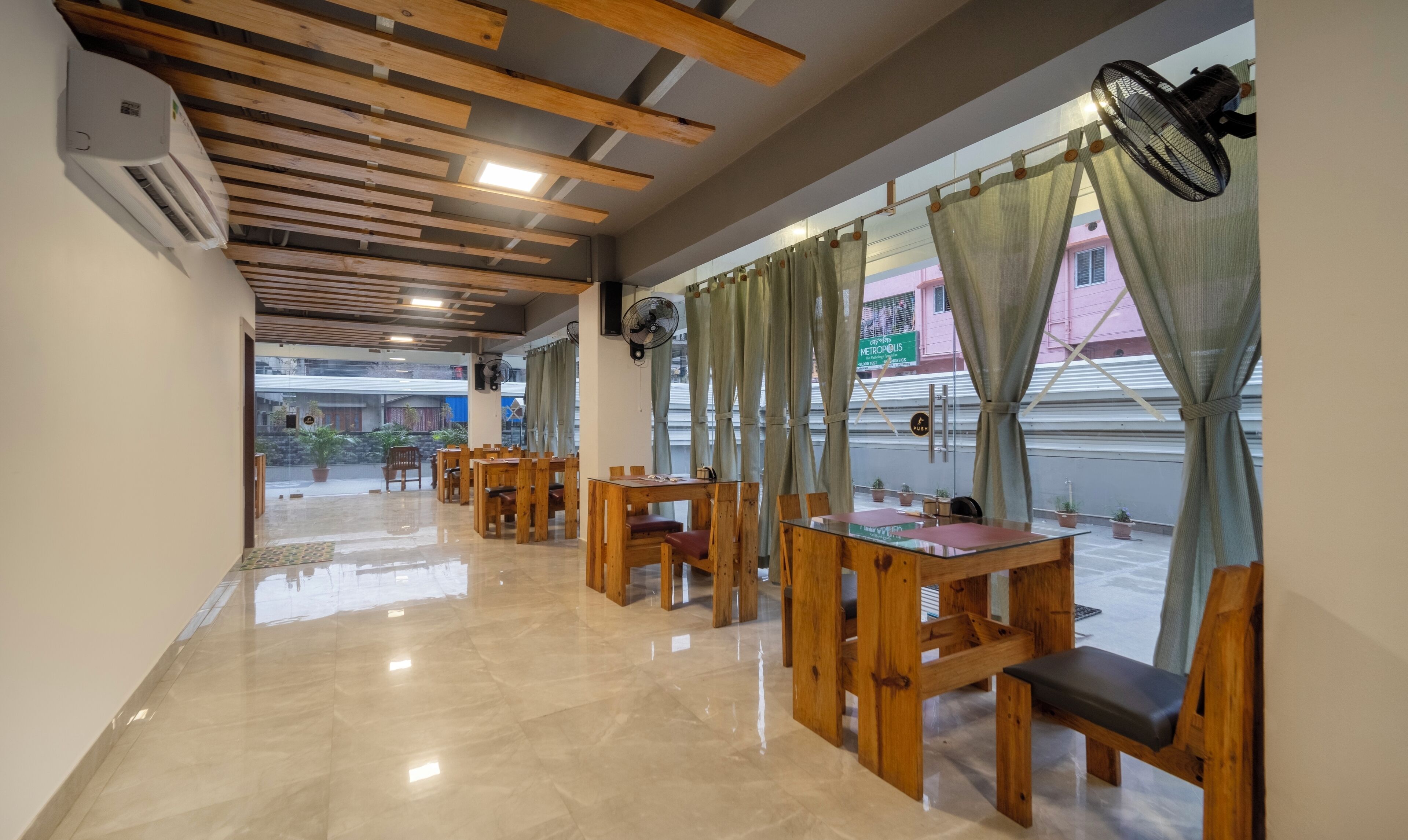 A restaurant interior with wooden tables and chairs, a tiled floor, and a view of the street outside.