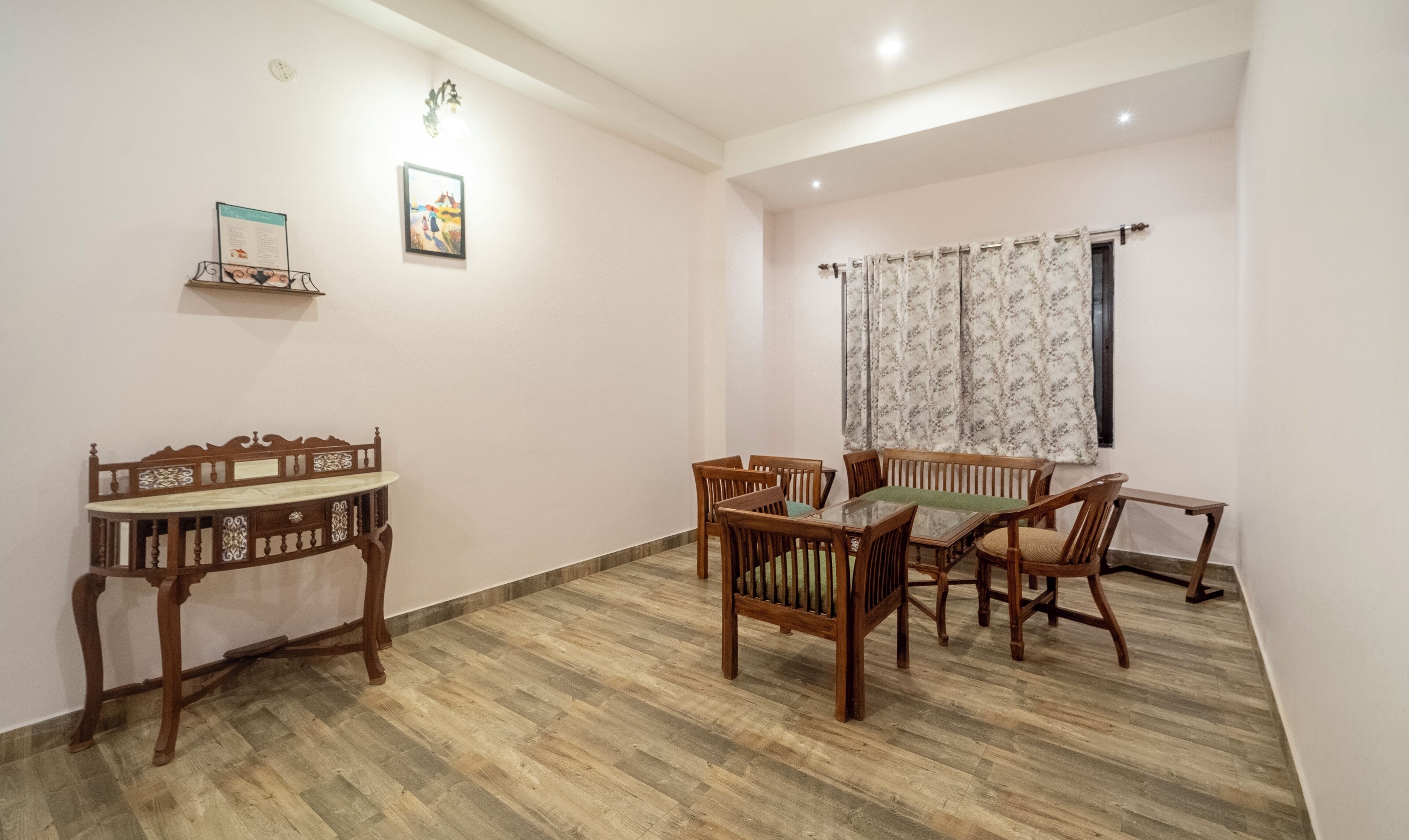 A dining area with a wooden table and chairs, a small wooden side table, and a wall-mounted shelf with a framed picture.