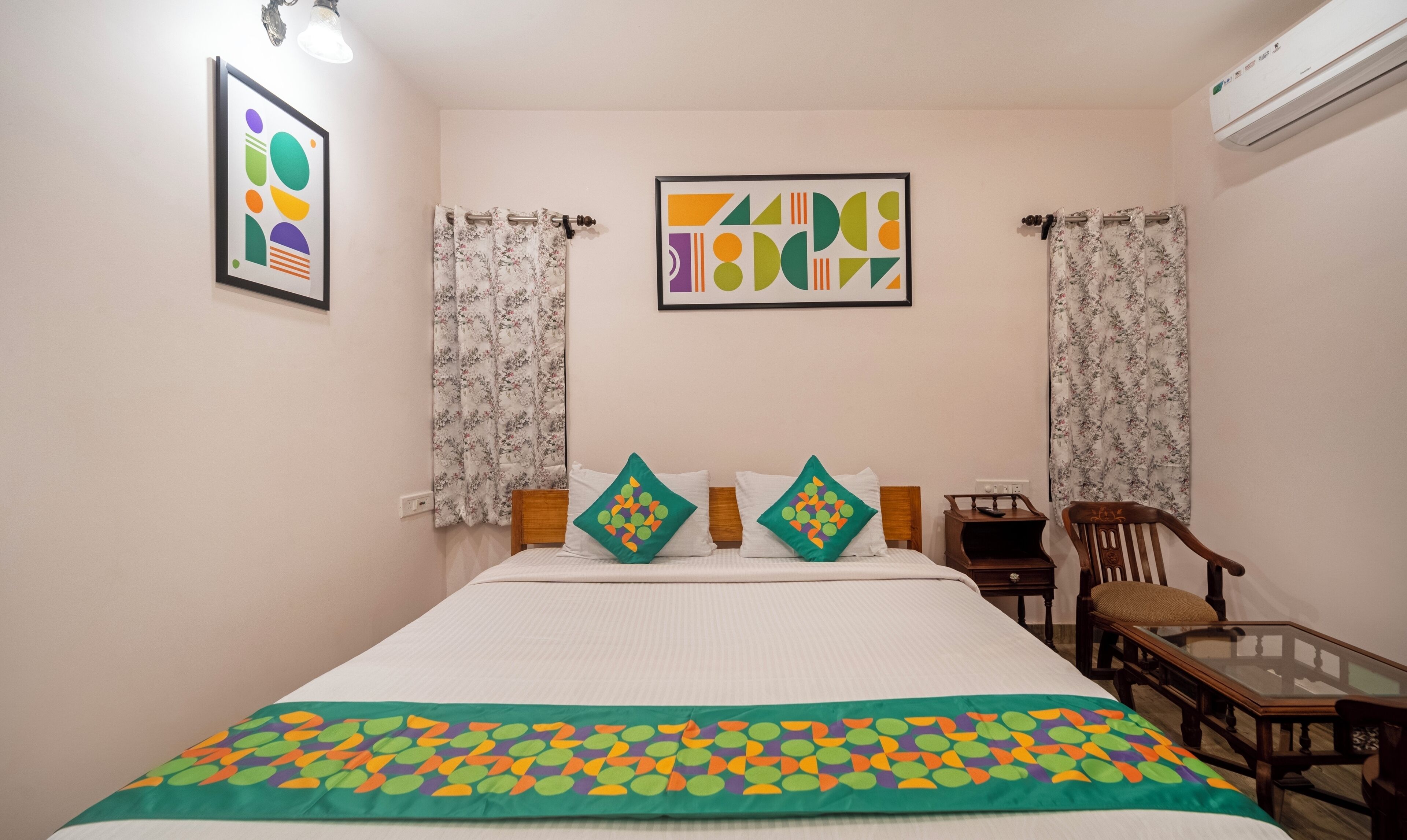 Une chambre d’hôtel avec un lit, une chaise, une petite table et deux œuvres d’art encadrées accrochées au mur.