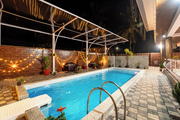 A swimming pool with a covered area, lounge chairs, and potted plants. -  Treebo Grand Royale Eco Residency with Pool (Benaulim)
