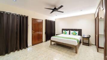 Un dormitorio con cama, cortinas, ventilador de techo, puerta de madera y una pequeña mesa con tetera.