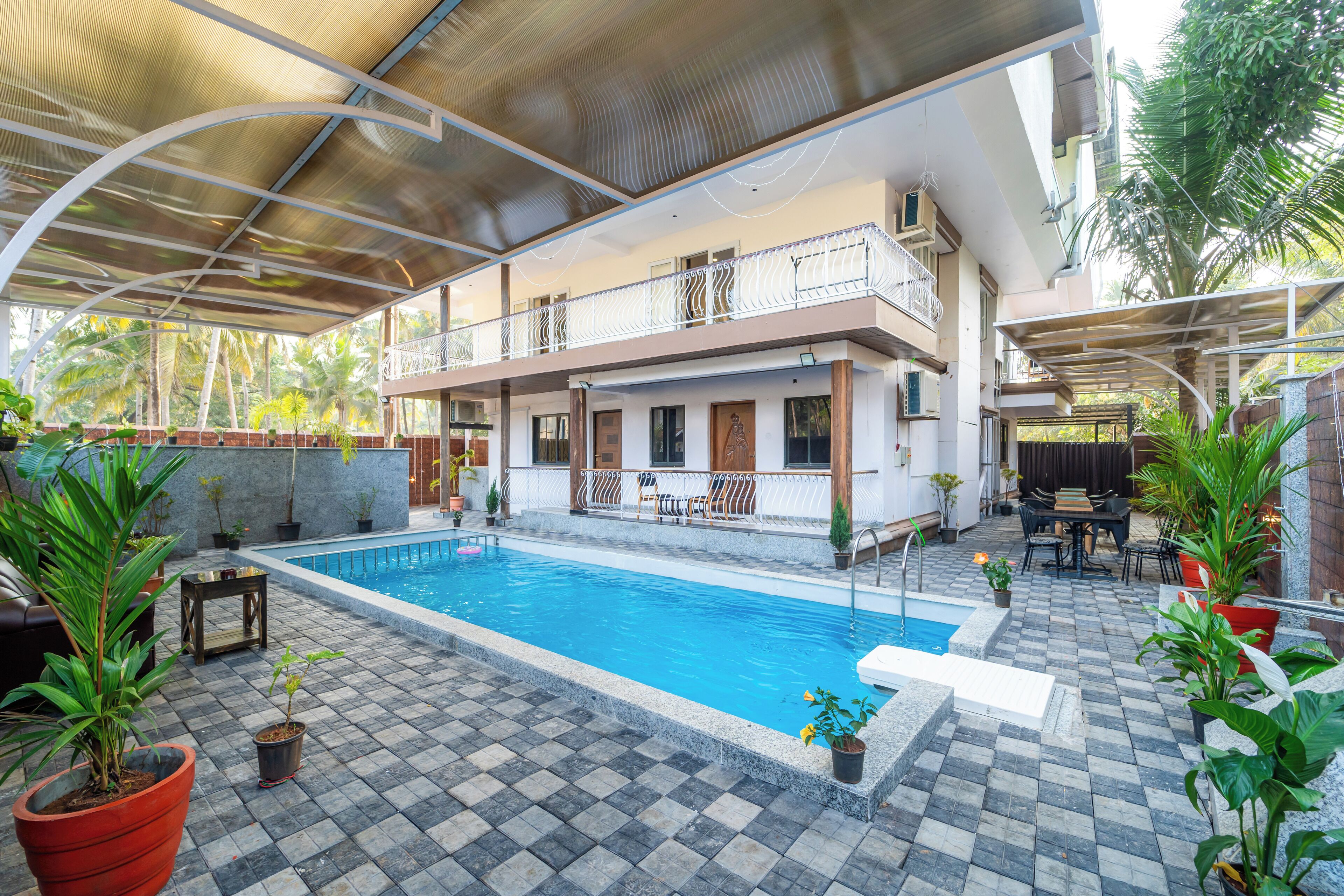 A two-story building with a swimming pool, outdoor seating, and potted plants.