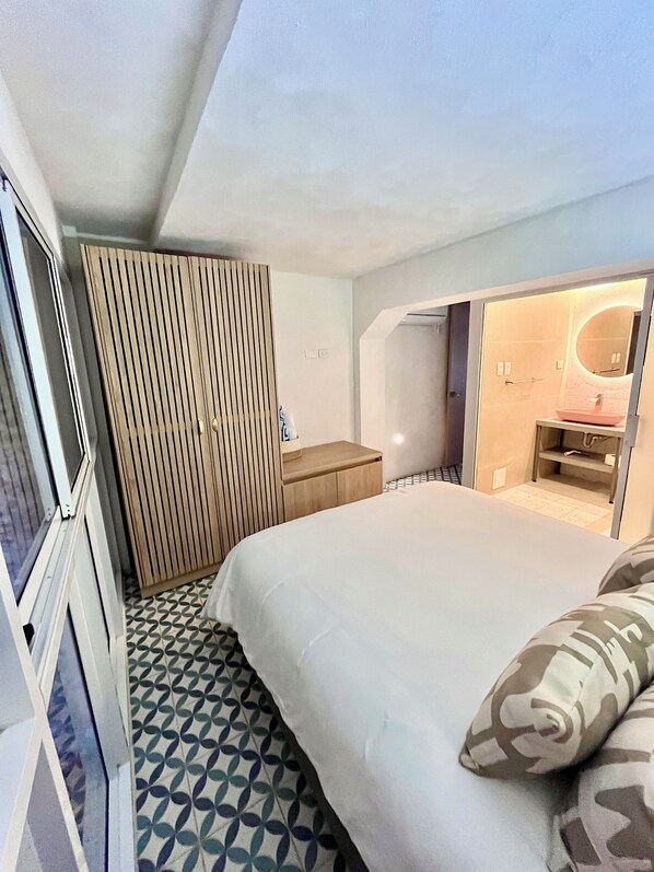 A bedroom with a bed, a wooden wardrobe, a bedside table, and a bathroom visible through an open door.
