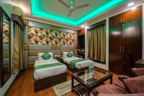 A hotel room with two beds, a ceiling fan, a wooden wardrobe, and a glass coffee table. - Treebo Marigold (New Delhi)