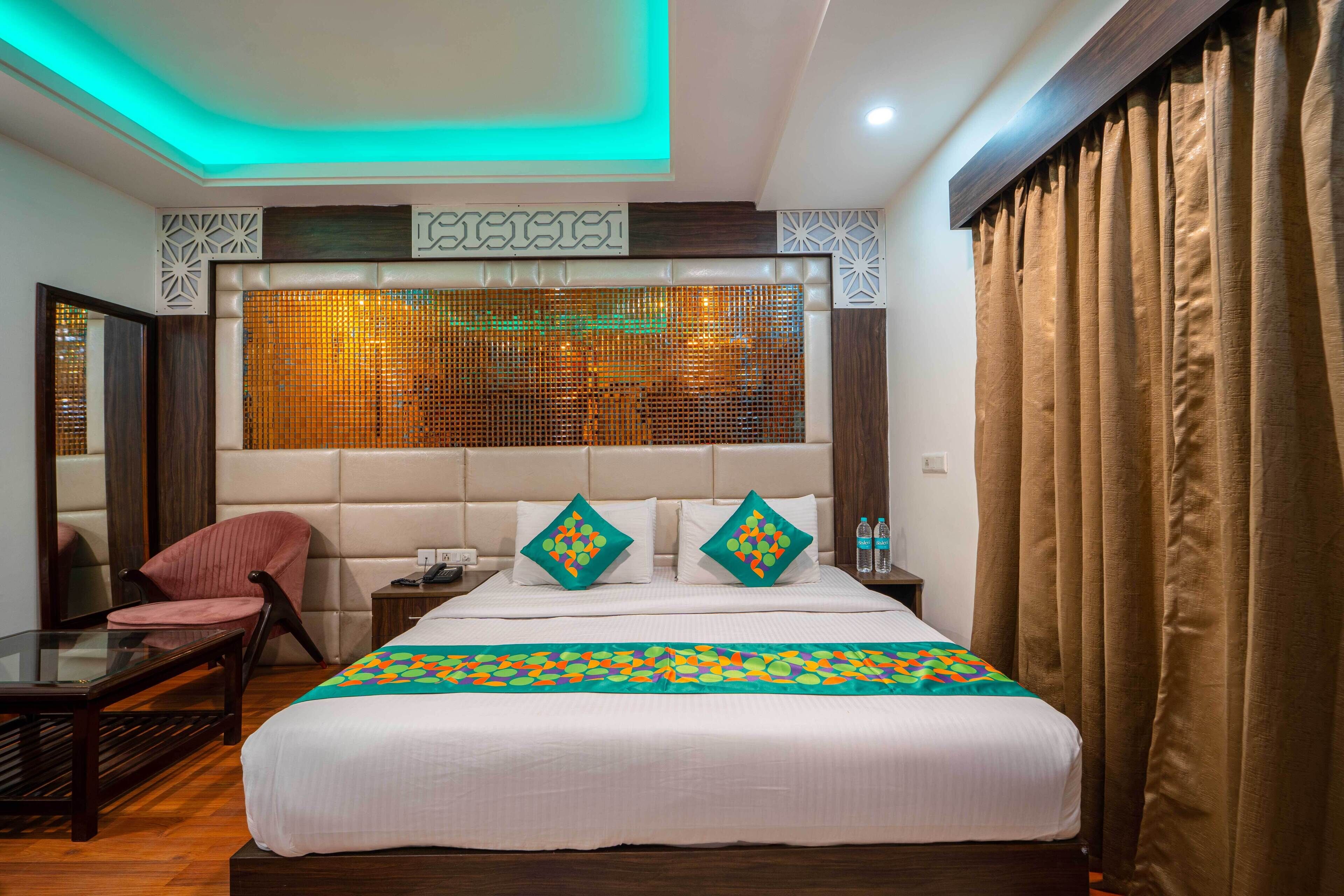 A hotel room with a large bed, a nightstand, a chair, and a mirror.