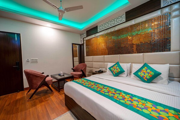 A hotel room with a bed, two chairs, a desk, and a ceiling fan. - Treebo Marigold (New Delhi)