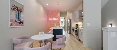 A modern kitchen with stainless steel appliances, a central island, and a dining area with a round table and pink chairs.