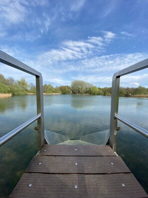 A wooden dock leading into a calm body of water with metal railings on either side. - Lovely forest Cottage for families or a group of friends! (Ewijk)