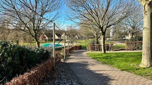 En asfalterad gångväg i en park med träd och en lekplats i bakgrunden.