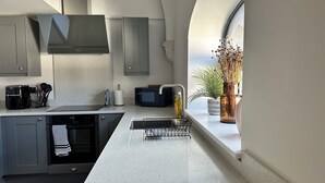 A modern kitchen with grey cabinets, a black coffee machine, a microwave, and a sink with a dish rack. - Charming 2-bedroom duplex apartment with WiFi in charming Norwich (Norwich)