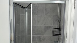 A glass-enclosed shower stall with a showerhead and a handheld shower attachment. - Charming 2-bedroom duplex apartment with WiFi in charming Norwich (Norwich)