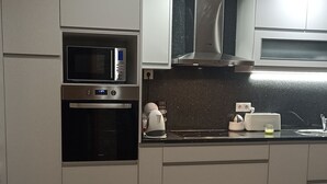 A modern kitchen with white cabinets, a built-in microwave, oven, and stainless steel range hood.