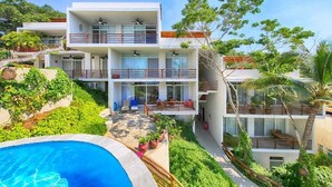 Un hotel moderno de varios pisos con piscina, abundante vegetación y balcones.