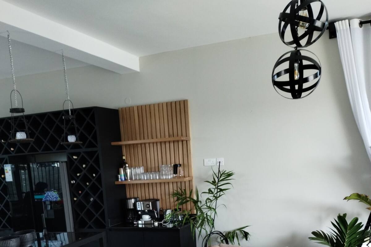 A modern living room with a sectional sofa, a coffee table, and a kitchen area with a wooden cabinet and hanging lights.