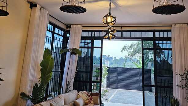 A modern living room with a sofa, large windows, and hanging light fixtures. - Muguet by Ibiscot Development (Entebbe)
