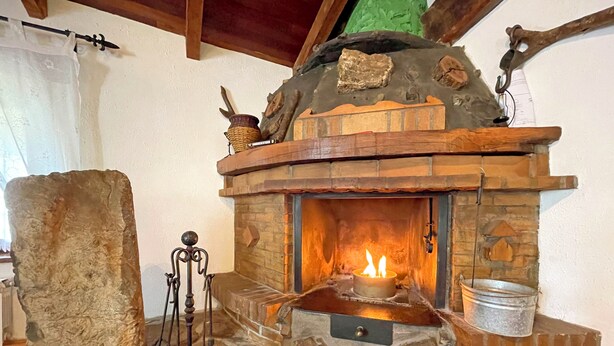 Un caminetto in pietra con un fuoco acceso, una panca in pietra e una scaffalatura in legno rustico.