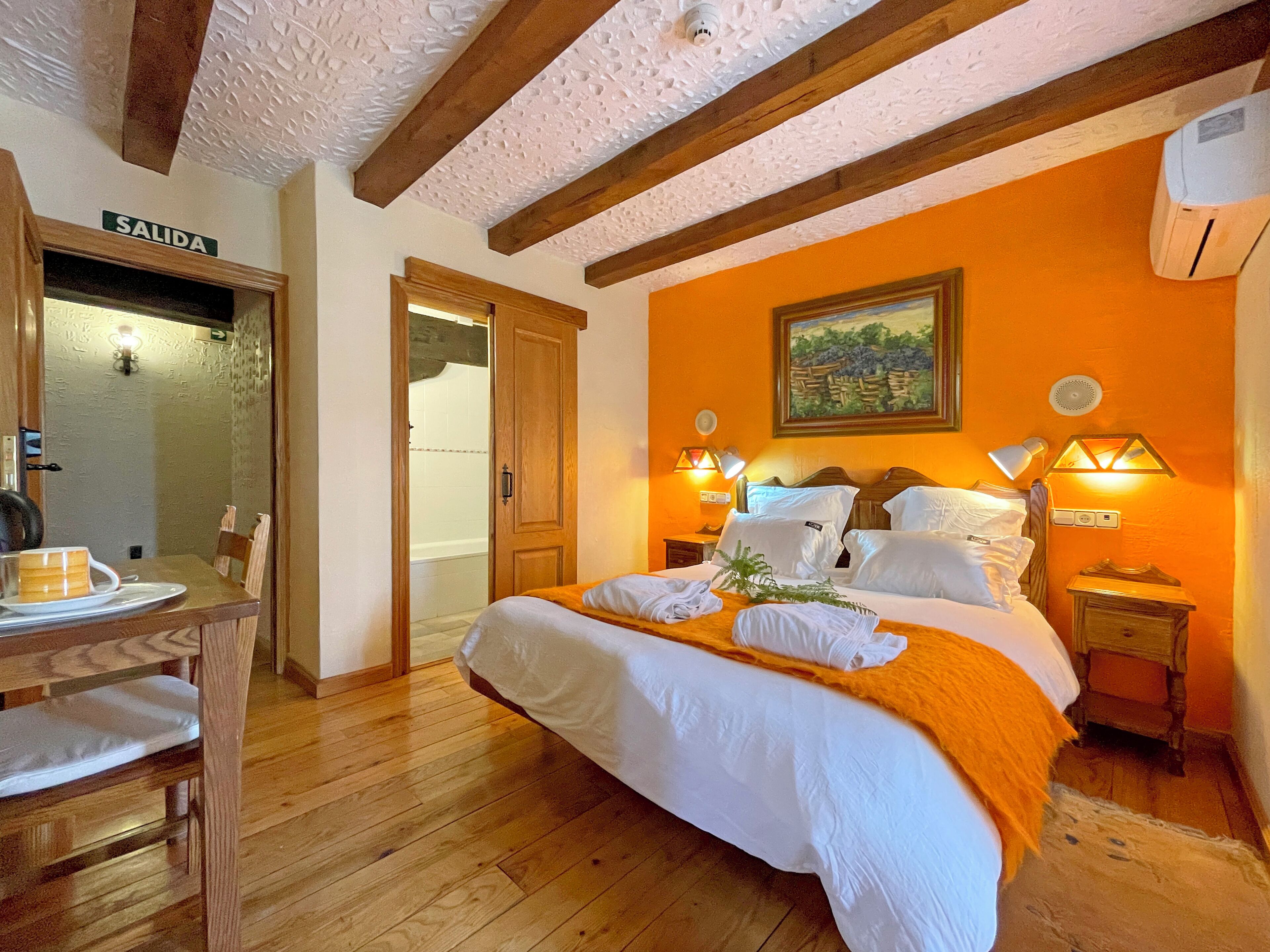 Ein Hotelzimmer mit einem Bett, einem Holztisch, einem Stuhl, einem Bild an der Wand und einer Klimaanlage.