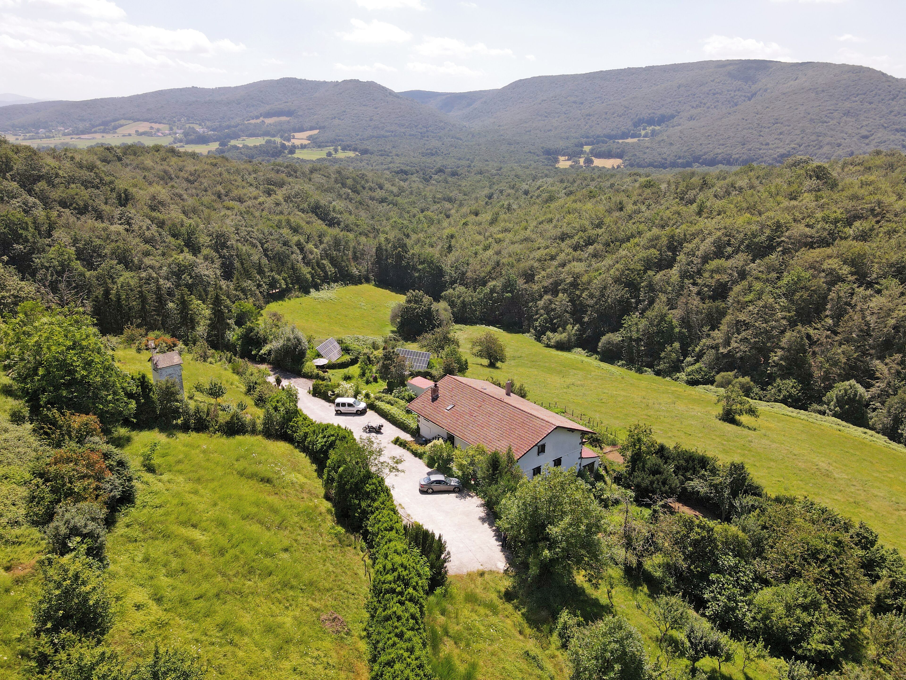 Uma propriedade rural com casa, entrada de automóveis e um carro estacionado na frente.