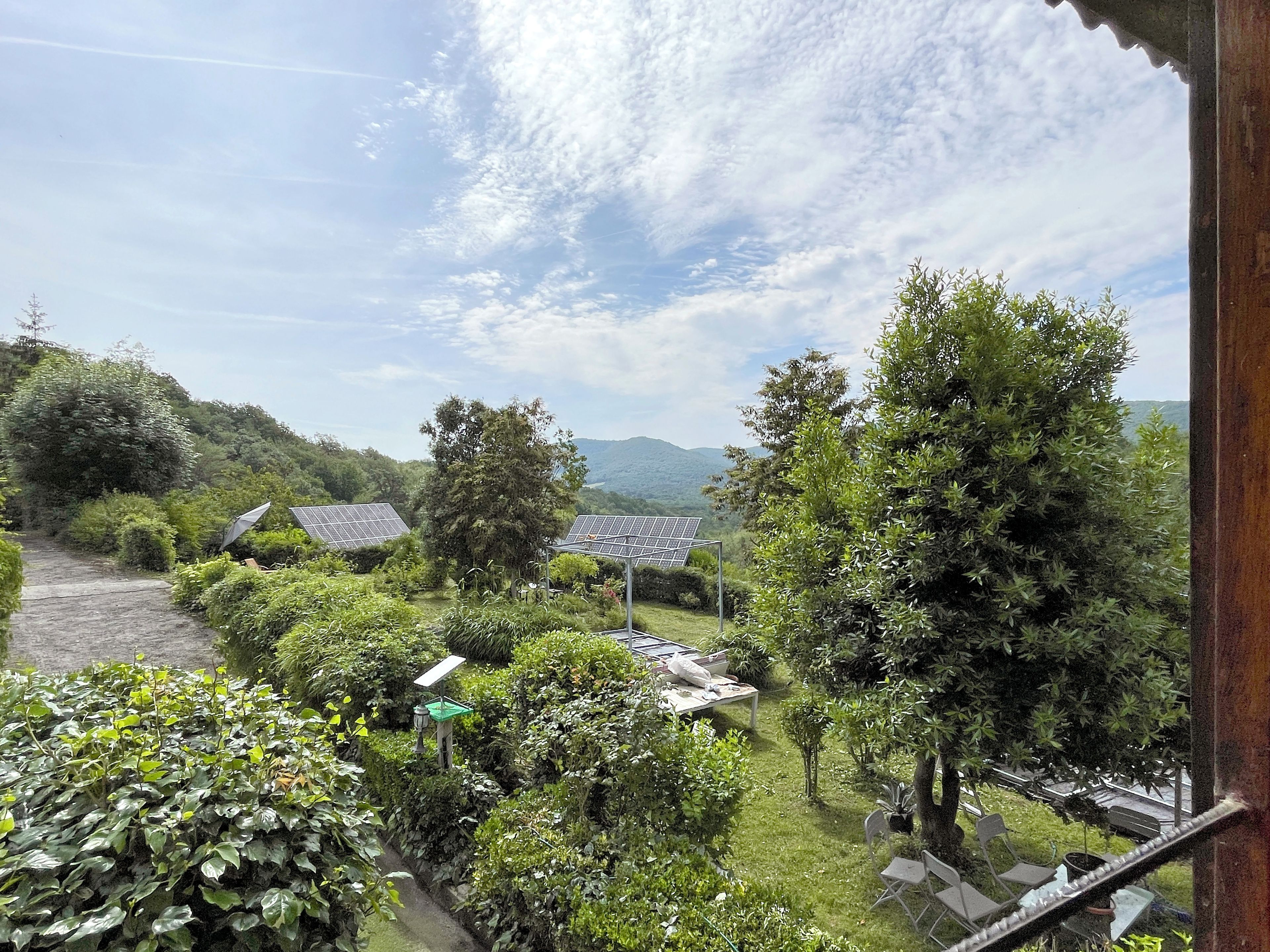 Un jardí exuberant amb panells solars, un camí de pedra i una vista a muntanyes llunyanes.