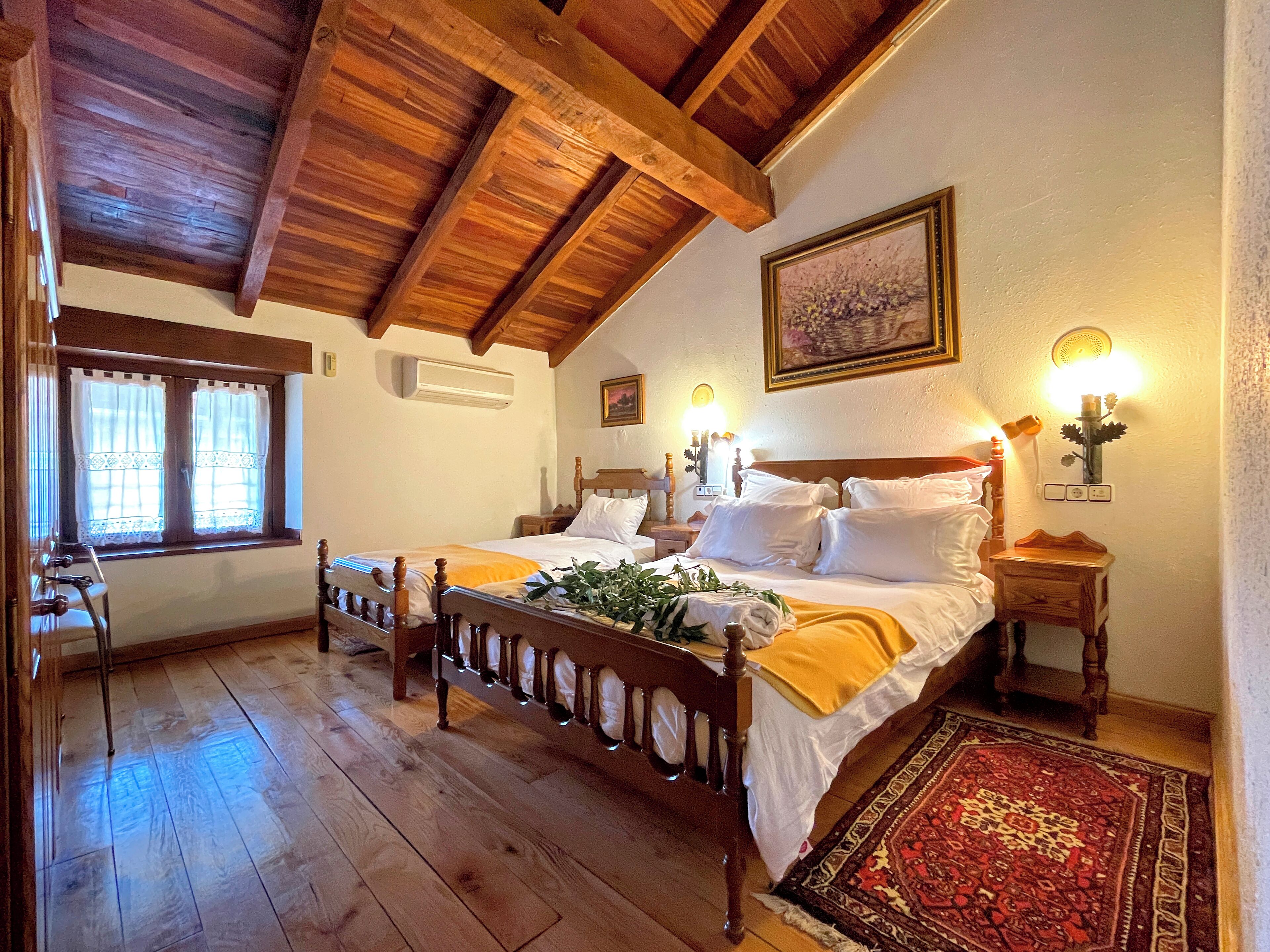 Un dormitorio con techo de madera, una cama grande con ropa blanca de cama, una mesita de noche con lámpara y una ventana con cortinas.