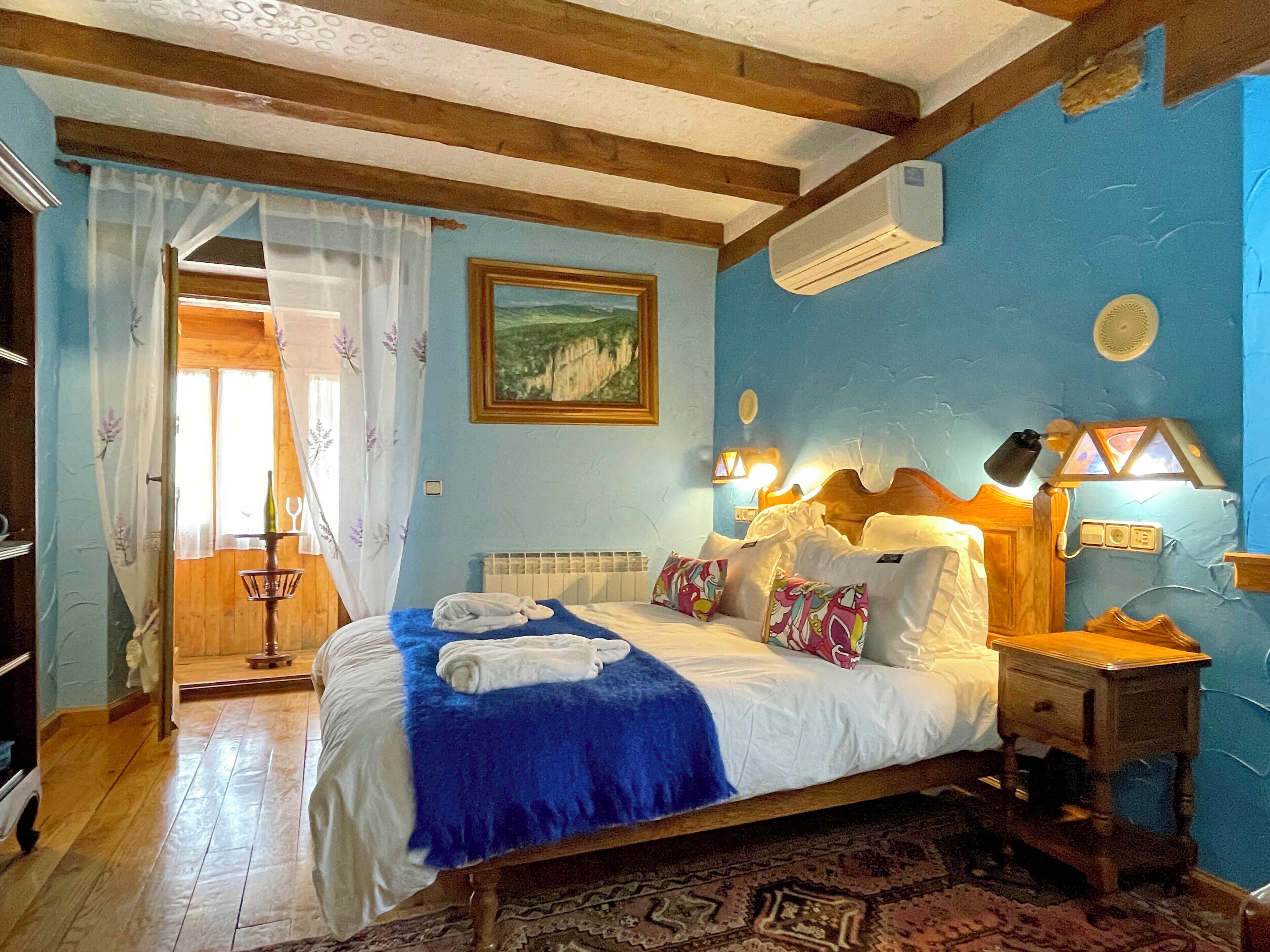 Une chambre à coucher avec un lit, une table de chevet, une lampe, un tableau et une fenêtre avec des rideaux.
