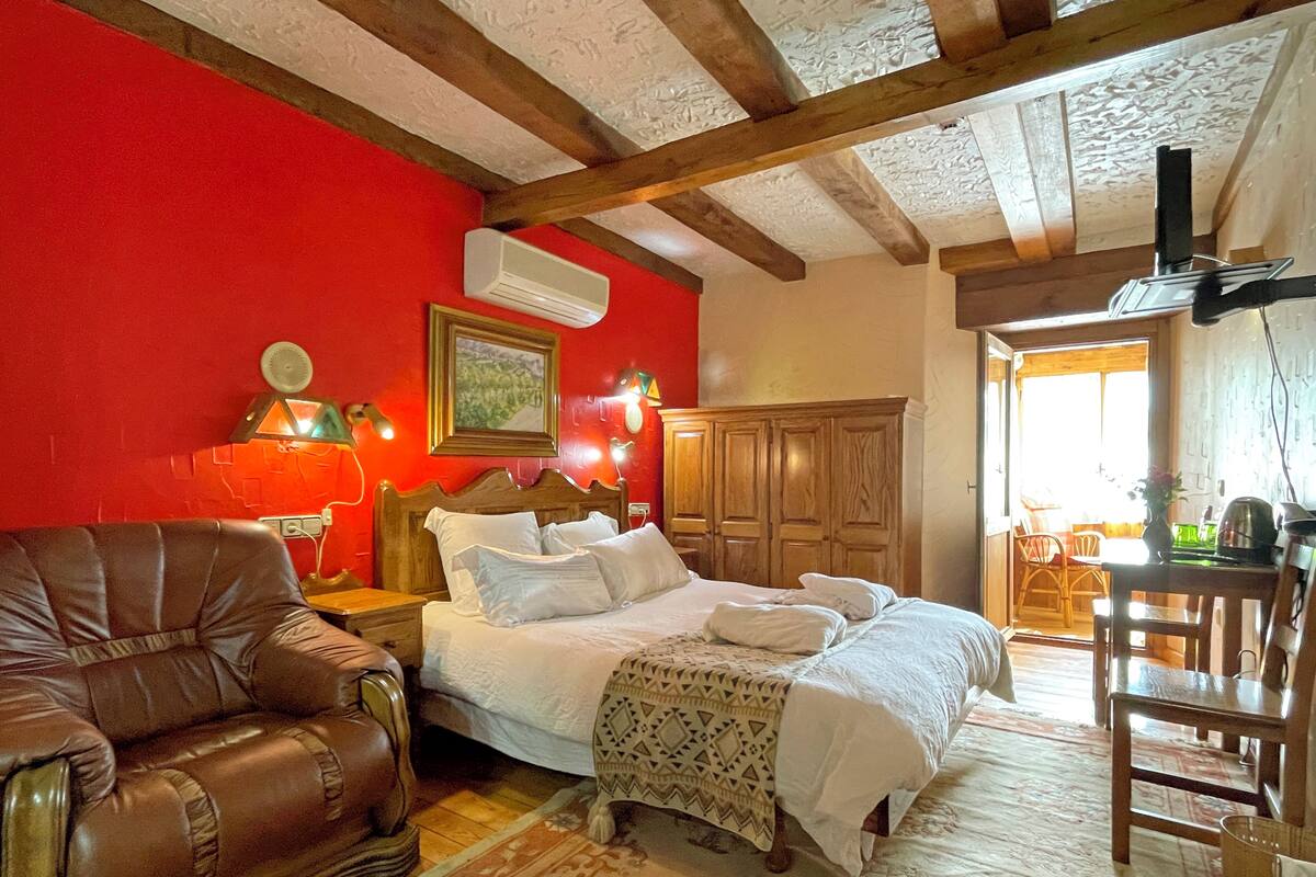 A cozy room with a bed, a leather armchair, a wooden wardrobe, and a dining area with a table and chairs.