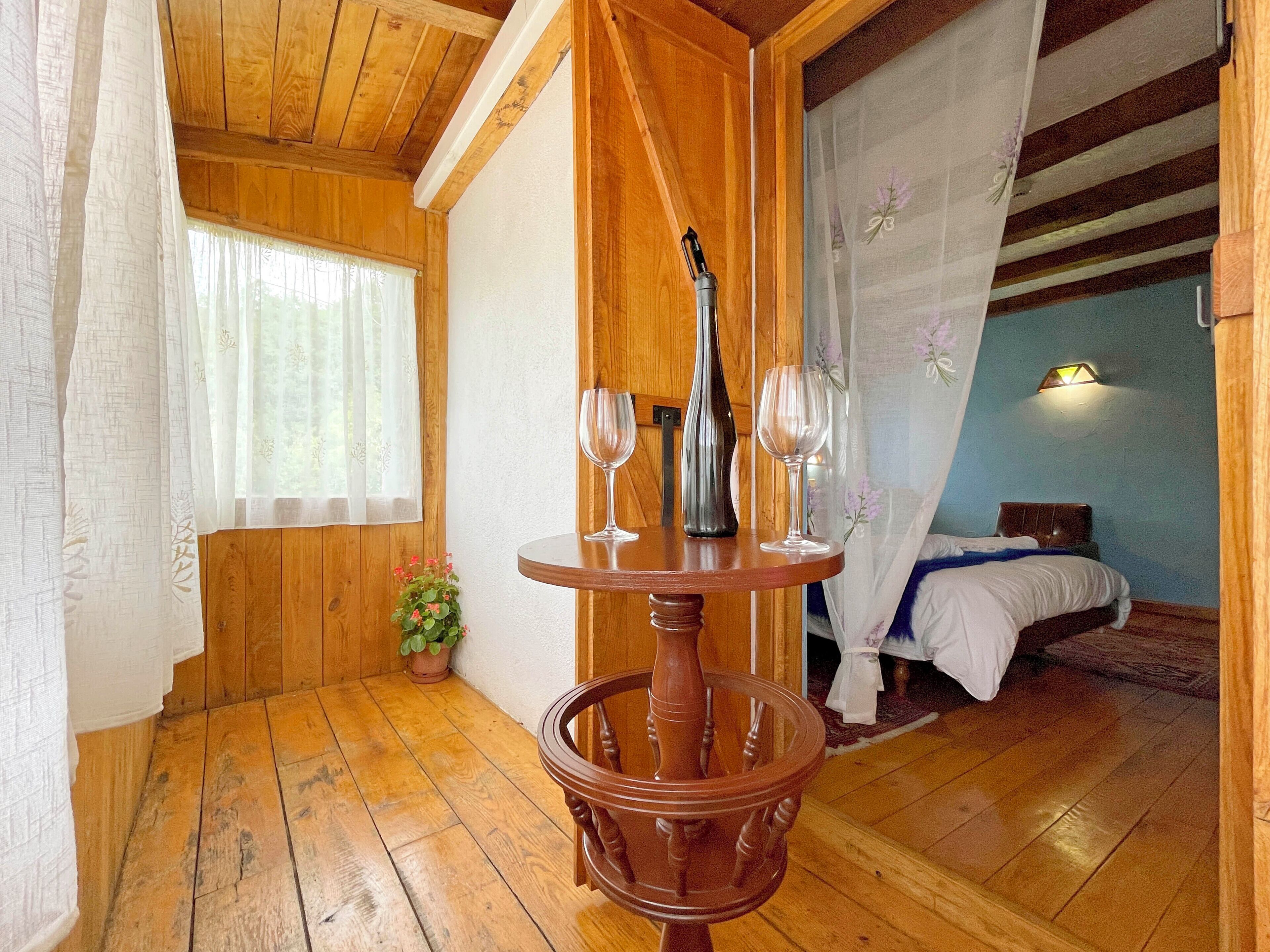 Une pièce en bois avec un lit, une table sur laquelle sont posés deux verres à vin et une plante en pot.