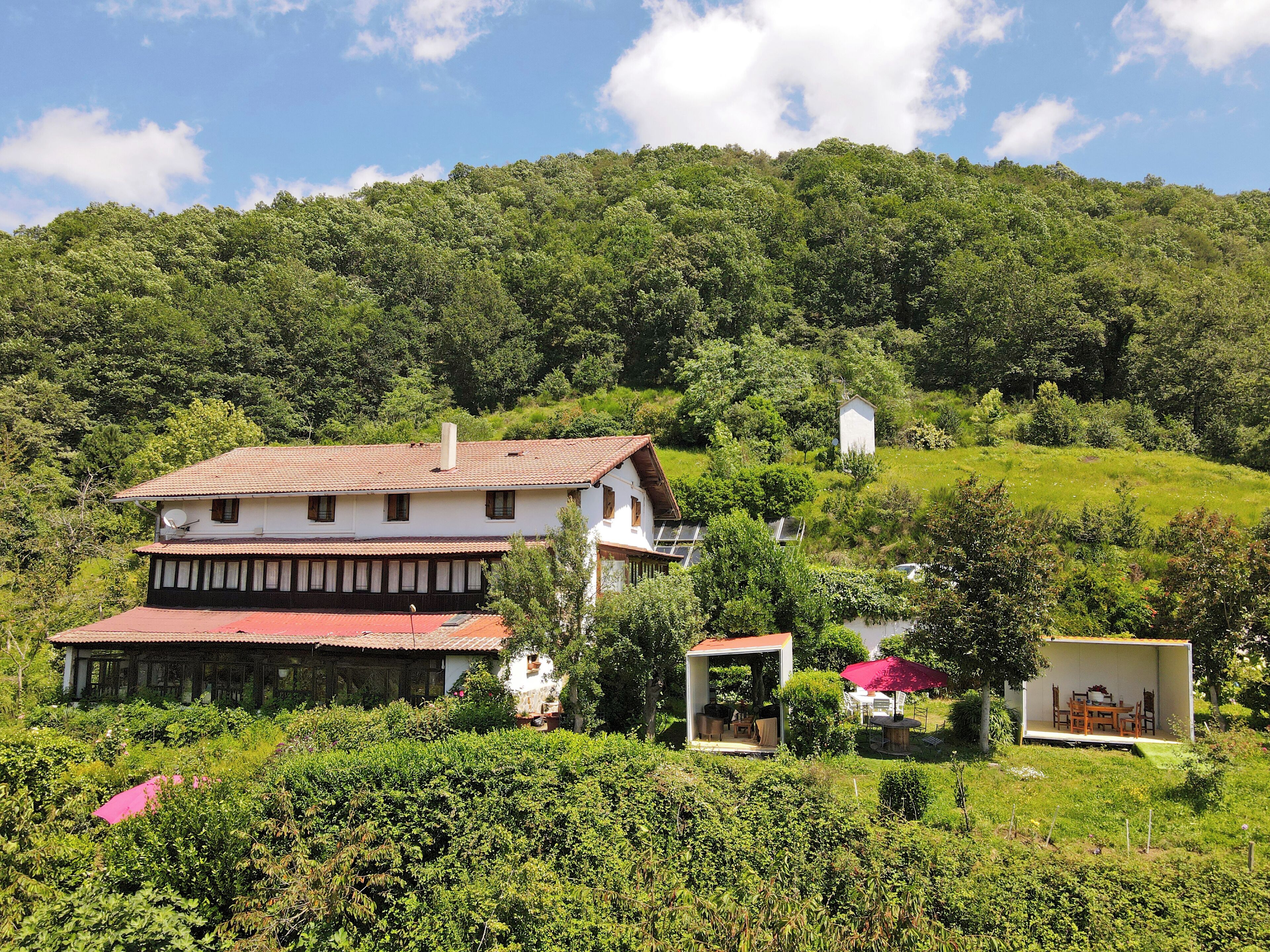 A traditional chalet with a sloped roof, a small annex, and a garden area with a red umbrella.