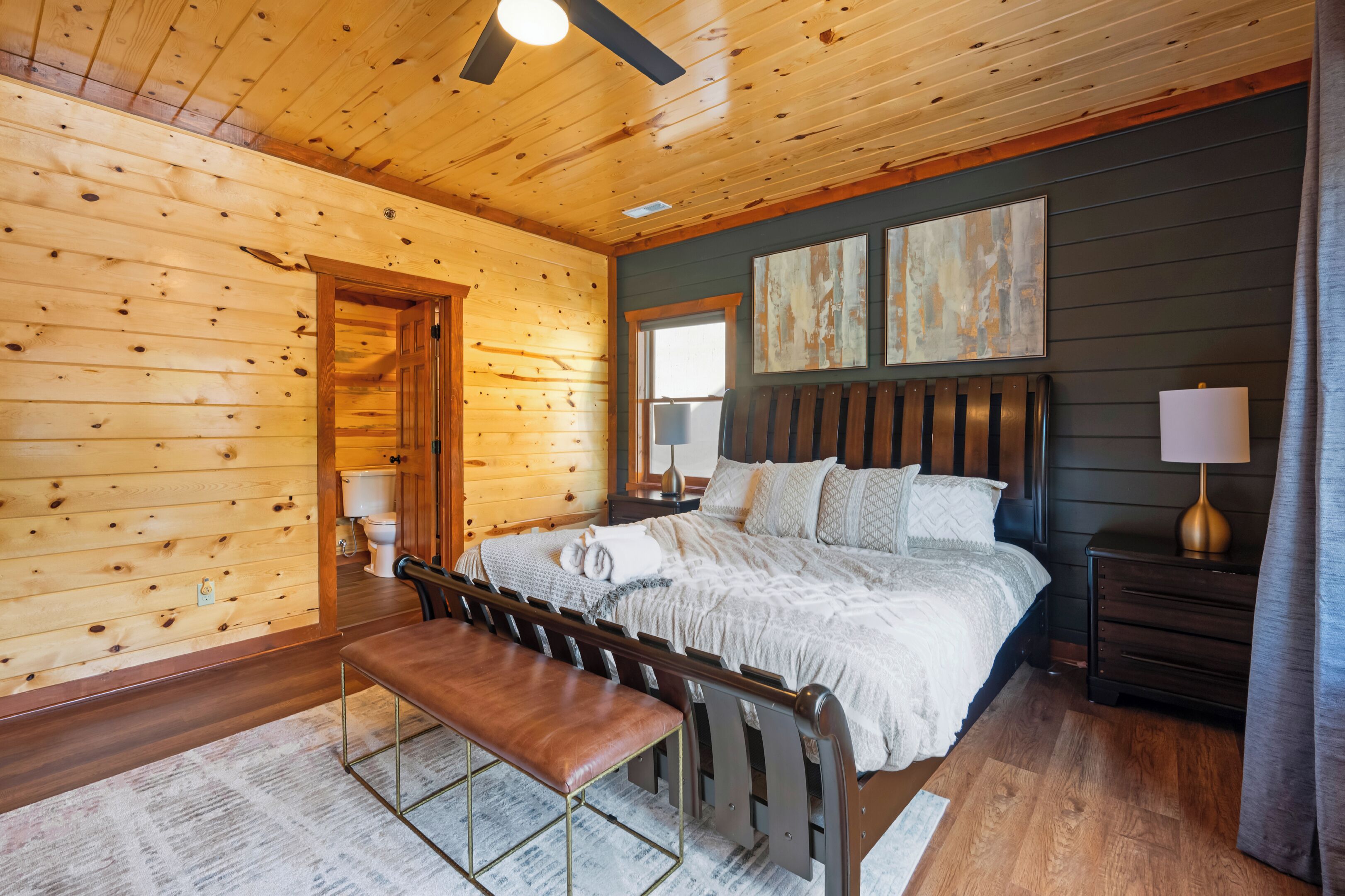 A cozy wooden cabin bedroom with a bed, bench, and artwork on the wall.