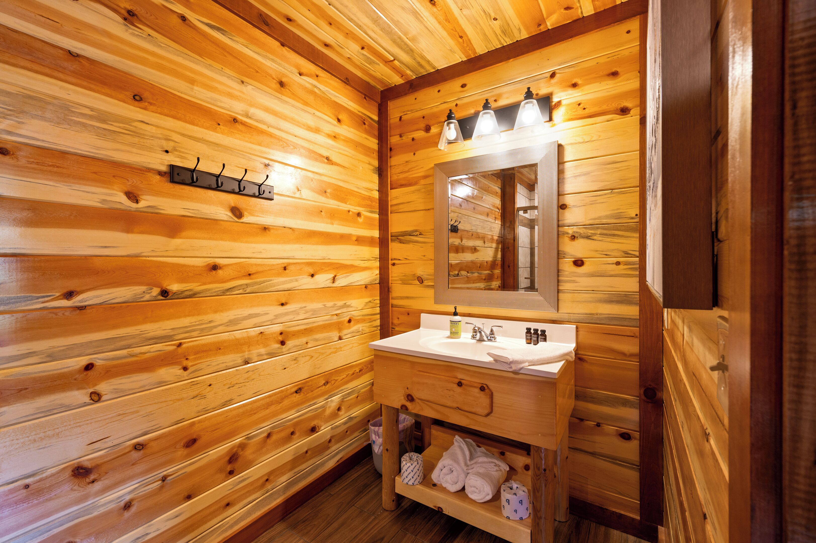 Ein Badezimmer einer Holzhütte mit einem Holzanrichte, einem Spiegel und einem Handtuchhalter.