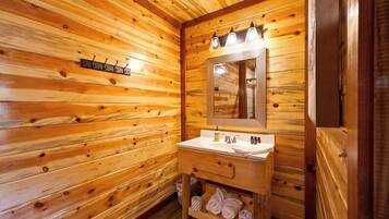 Ein Badezimmer einer Holzhütte mit einem Holzanrichte, einem Spiegel und einem Handtuchhalter.