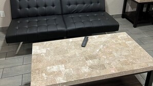 A black leather sofa with a remote control on a marble-topped coffee table.