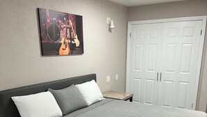 A bedroom with a bed, a nightstand, a dresser, a door, and a wall-mounted picture.