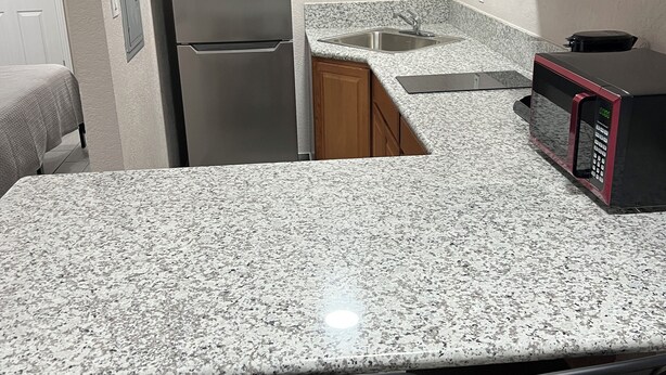 A compact kitchen with granite countertops, a stainless steel refrigerator, a microwave, and a sink.