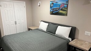 A bedroom with a bed, two bedside tables, a nightstand, a painting on the wall, and a closet.