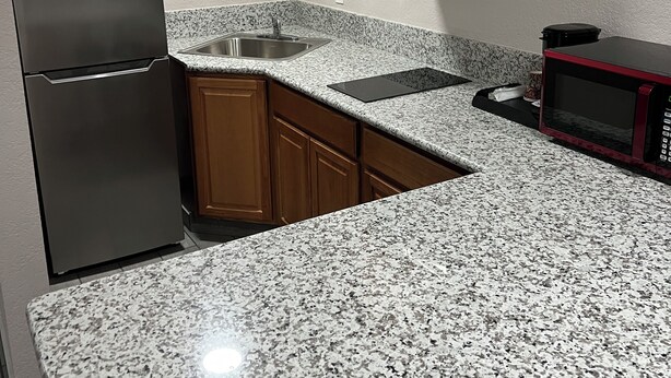 A kitchen with granite countertops, wooden cabinets, a stainless steel refrigerator, a microwave, and a built-in oven.