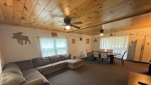 Una sala de estar acogedora con un sofá modular, una mesa de comedor con sillas y ventiladores de techo.