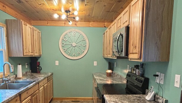 Una cocina con armarios de madera, piso de baldosas de piedra, un reloj en la pared y un cubo de basura.