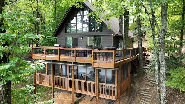 A two-story cabin with a deck, surrounded by trees. - Serene Cabin - Incredible VIEWS, 3 Bedrooms, 3 Bathrooms, Family & Pet-Friendly! (Deep Gap)