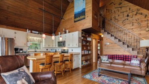 A spacious living area with a wooden staircase, a kitchen with white cabinets, and a dining area with a wooden table and chairs. - Serene Cabin - Incredible VIEWS, 3 Bedrooms, 3 Bathrooms, Family & Pet-Friendly! (Deep Gap)