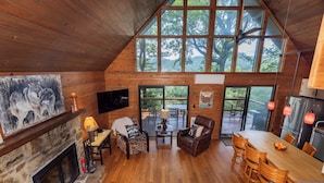 A cozy cabin interior with a fireplace, wooden floors, a dining area, and large windows offering a view of the outdoors. - Serene Cabin - Incredible VIEWS, 3 Bedrooms, 3 Bathrooms, Family & Pet-Friendly! (Deep Gap)