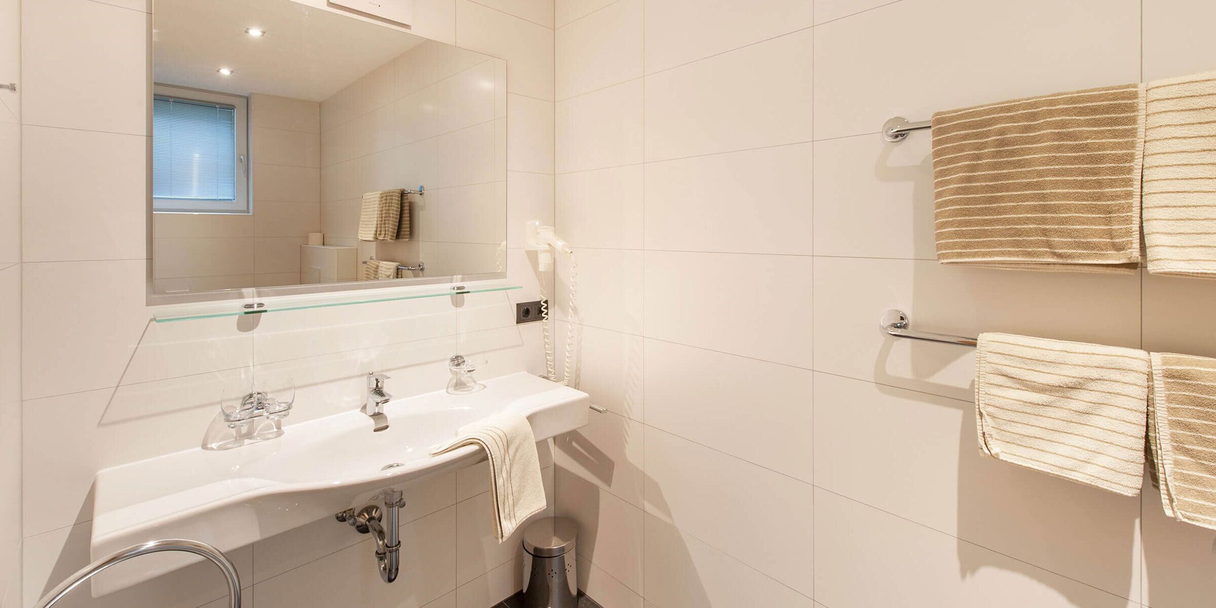Une salle de bain moderne avec un lavabo entouré de parois en verre, un miroir et deux serviettes suspendues à un porte-serviettes.