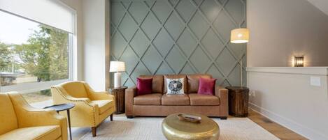 Ein Wohnzimmer mit einem braunen Sofa, gelben Sesseln, einem runden Couchtisch und einem gemusterten Teppich.