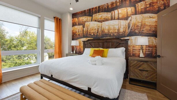 A bedroom with a large bed, a bench, a ceiling fan, and a mural of barrels on the wall.