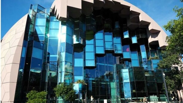 Un edificio moderno con una fachada geométrica única, amplios ventanales de vidrio y una entrada central con escalones.