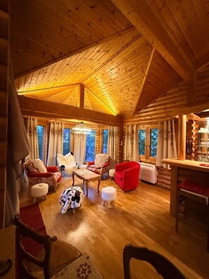 Interior de una cabaña de troncos con techo de madera, varias zonas de estar y una mesa de comedor.