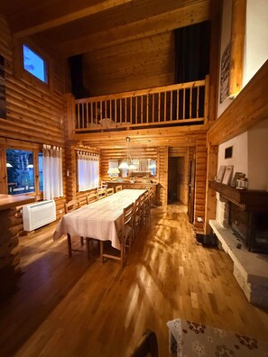 Interior de una cabaña de troncos con comedor, cocina y chimenea.