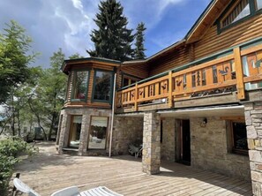 Una baita con fondamenta in pietra, un'area esterna in legno e un balcone con ringhiere decorate.